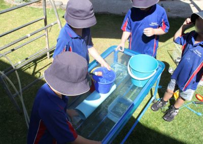Three students playing with containers filled with water at the school yard